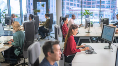 Side view of customer service representative talking on microphone while working on desktop computer in call centre.